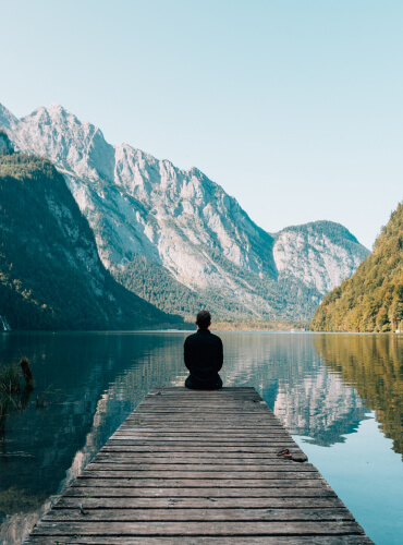 Homme assis sur un ponton sur un lac en montagne